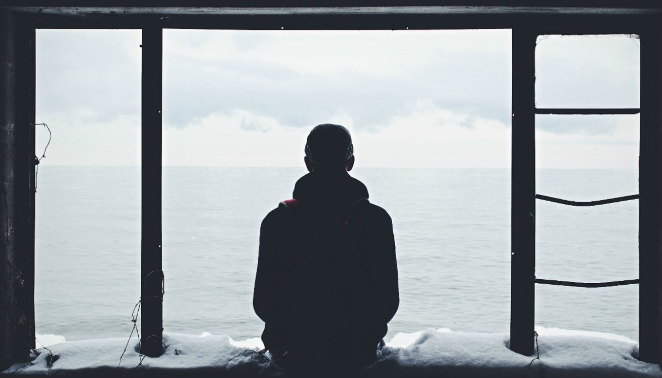 A man sitting on a snowy windowsill looking out at the water